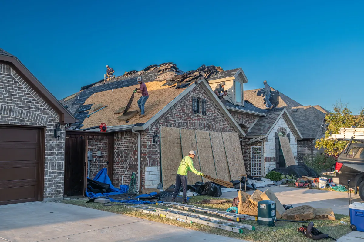 Before: old roof mid tear-off with debris on the lawn of a brick home