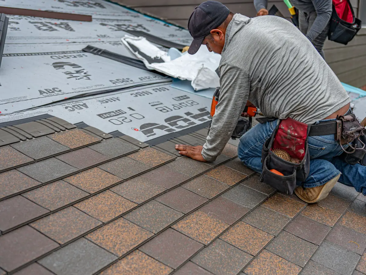 Roofer kneeling on a roof and hand-placing replacement shingles during a repair