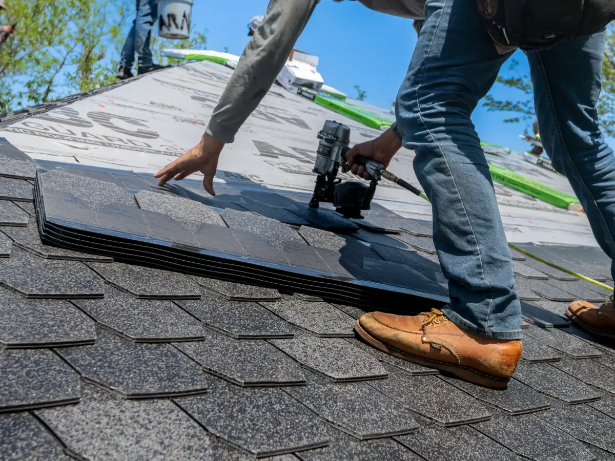 Roofer nailing new architectural asphalt shingles during a full roof replacement